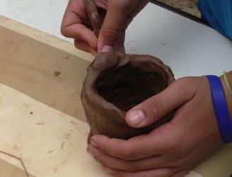 Fotografía de detalle con las manos de un niño manipulando barro para hacer un cuenco