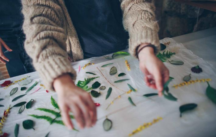 Estampación botánica: Manos colocando hojas y flores sobre un tejido.