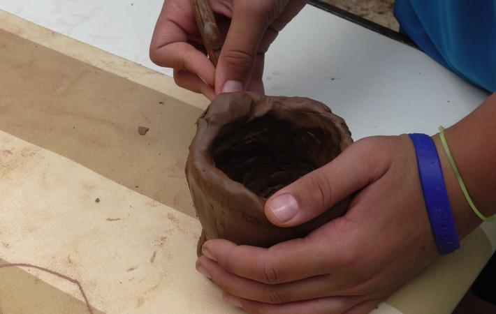 Fotografía de detalle con las manos de un niño manipulando barro para hacer un cuenco